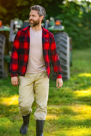 Crop harvesting. Agriculture equipment. Farmer with harvesting machinery. Mature man at tractor. Tractor driver. Agriculture and field work. Farmer wear gum boots walking at tractor outdoorの写真素材