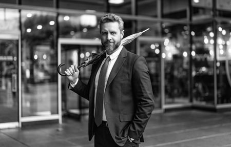 Successful Hispanic businessman man in business suit hold umbrella standing at the office outdoor