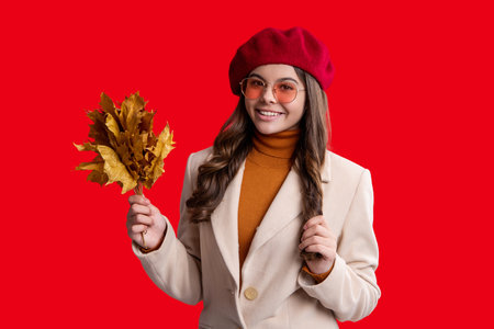 Fallen autumn leaves. September season. Stylish teen girl isolated on red with maple leaf. Autumn leaf arrangement. Girl with maple leaf wear hat. Fall season beauty. Autumn style fashionの写真素材