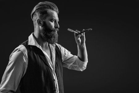 Bearded hipster barber isolated on black. Man beard haircut by hairdresser at barbershop. Handsome barber using retro blade while cutting hair. Modern barbershop haircut. Copy spaceの写真素材