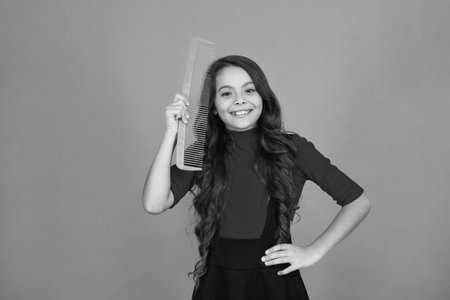 Teen girl combing curly hair. Girl with hairbrush isolated on orange. Teen beauty hairstyle. Haircare. Girl use hair comb. Comb and hairbrush. Brushing hair. Taking careの写真素材