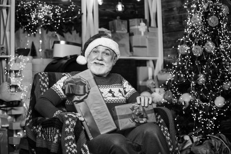 Traditions concept. Elderly grandpa at home. Delivering gifts. Presents for family. Santa Claus relaxing in arm chair. Bearded senior man Santa Claus. Legend about Santa Claus. Merry christmasの写真素材