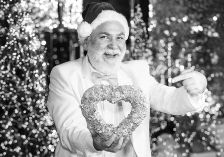 this winter may be joyful. senior santa in tuxedo on christmas lights background. garland new year decoration. gift with love. happy businessman decorative heart. he loves xmas holidaysの写真素材