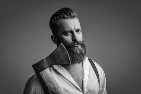 Masculine man. Masculinity of bearded man with axe isolated on grey. Caucasian brutal man with beard and moustache. Masculine energy. Retro style. Handsome and charismaticの写真素材
