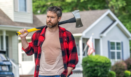 Lumberjack at his house with ax. Lumberjack tired with heavy axe. Strong man work in the backyard. Man with axe. Lumberjack carries axe. Mature sweating man with axe, copy spaceの写真素材