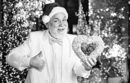 Real feelings. senior santa in tuxedo on christmas lights background. garland new year decor. gift with love. happy businessman decorative heart. he loves xmas holidays. this winter may be joyfulの写真素材