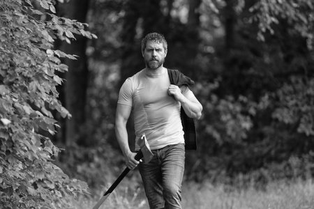 Lumberjack carries axe. Hardworking man. Handsome man with axe. Lumberjack in woods with an ax. Lumberjack in shirt with heavy axe. Strong man work in forest. Lumberjack in forest with axeの写真素材