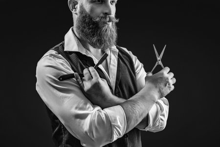 Modern barbershop haircut. Bearded hipster barber isolated black. Man beard haircut by hairdresser at barbershop. Handsome barber using retro blade and scissors while cutting hair. Barber expertiseの写真素材