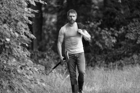 Lumberjack in woods with an ax. Lumberjack in shirt with heavy axe. Strong man in forest. Lumberjack carries axe in forest. Lumberjack sweating after hardworking. Mature man with axeの写真素材