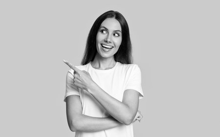 Woman in white tshirt isolated on yellow. Amazed young woman point finger. Stylish female. Advertisement offer. Portrait of millennial girl. Millennial girl presenting productの写真素材