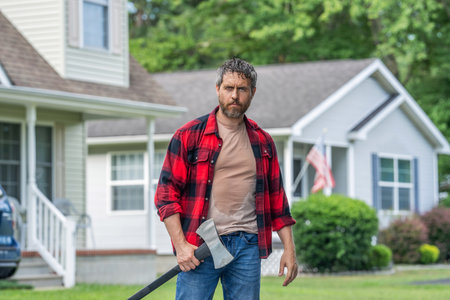 Lumberjack tired with heavy axe. Strong man work in the backyard. Man with axe. Lumberjack carries...