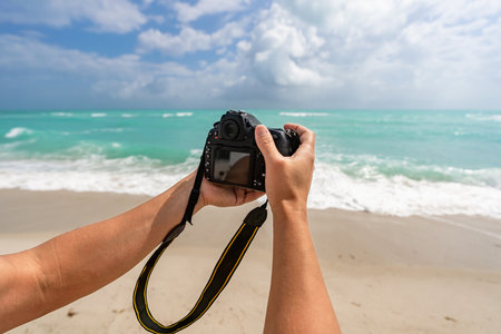 Photo camera at beach. Summer beach vacation. Traveling and photography. Photographer making photo with camera. Traveler with camera on summer beach. Travel photography. Travel in summerの写真素材
