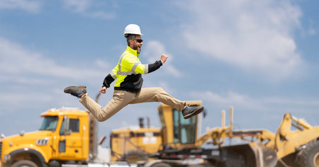 Excited construction builder. Worker jumping at heavy machines. Man engineer running to success. Builder man run fast to work. Engineer supervisor running outdoor. Supervisor jumping. Copy spaceの写真素材
