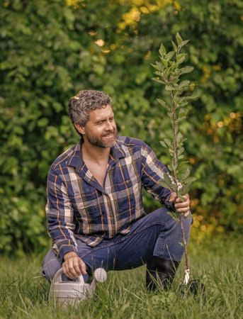 Planting forest. Man with watering can in garden. Watering tree. Planting a tree. Gardening and watering orchard. Seedling for planting tree. Gardener man gardening. Gardener in springの写真素材