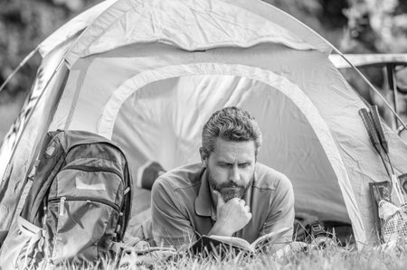 Man hiker outdoor on summer day. Summer camp and nature vacation. Man relax on summer camping. Camp adventure. Hiking retreat. Camping tent. Reading book. Man read book at camp in forestの写真素材