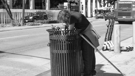 San Diego, California, USA - May 17, 2019: Homeless man beggar rummaging through trash outdoor. Poor man rummage in the garbage in search of food. Poverty and hunger. Hungry man rummage at trashのeditorial素材