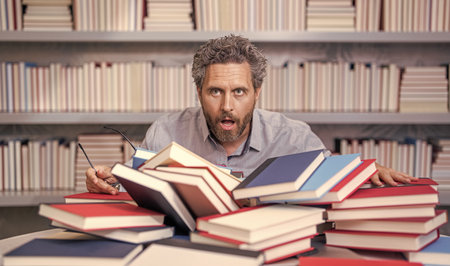 school education in college. knowledge day. overwork of bookworm. tired teacher genius in school library. genius studying homework literature near pile of books. man teacher read book. do homeworkの写真素材