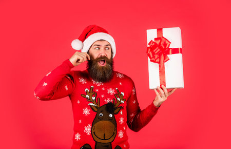 What a great surprise. ready for party celebration. morning before Xmas. bearded man in sweater. hipster enjoy the holiday. new year shopping idea concept. man in santa hat await christmas presentの写真素材