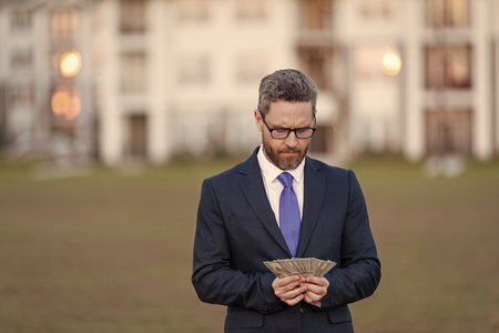 Successful realtor in suit with money dollar. House owner hold money outdoor. Realtor offering new home. Broker make offer. Businessman broker count money. Property concept. Copy spaceの写真素材