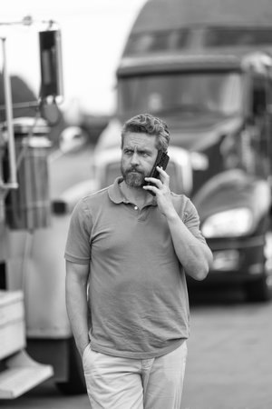 Trucking owner. Transportation vehicles. Hispanic man posing in front of truck. Man owner truck driver. Man driver talk on phone near lorry truck. Truck driver has phone callの写真素材