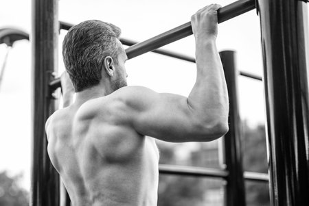 Muscular biceps and triceps. Strong athlete. Man pullup at outdoor gym. Muscular man sportsman with...
