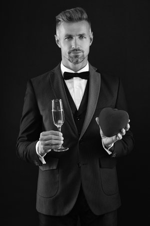 Happy valentines day. Man with love isolated on black . Love romantic gift. Rich man in tuxedo with champagne. Rich man celebrate valentine day. Man with heart. Engagement dayの写真素材