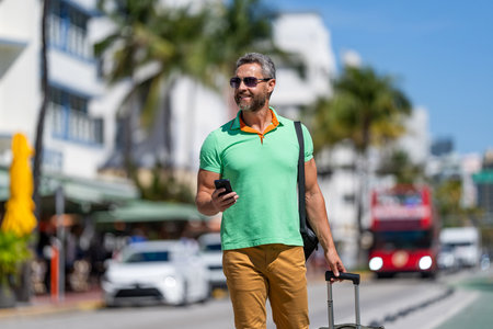 Tourist with travel bag. Traveler using phone. Tourist booking vacation trip. Traveler suitcase for summer trip. Man booking summer trip. Hispanic tourist traveler book online outdoor. Calling taxiの写真素材