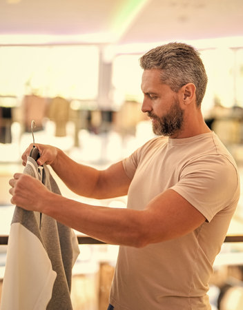 Casual style menswear in luxury store. Luxury boutique shopping for a stylish man. Male fashion shop. Stylish man in menswear boutique. Mature man choosing shirt. Designer clothing. Outfit ideasの写真素材