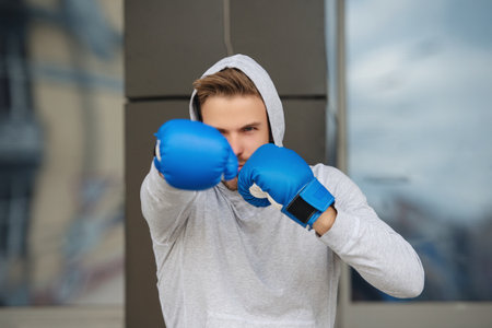 Strong boxer in sportswear. Exercising and punching. Practicing boxing. Sportsman in boxing gloves outdoor. Young man boxer. Sport man boxing. Strong athlete man. Sportsman in hoodie. Ring movementの写真素材