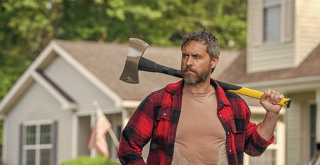 Lumberjack at his house with ax. Lumberjack sweating hold heavy axe. Strong man work in...
