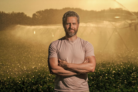 Man at irrigation system watering agricultural field. Farmer man in countryside. Water sprinkler irrigating crop field. Drip irrigation system. Crop irrigation. Agriculture and farming. Water processの写真素材