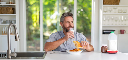 Business man eating morning breakfast. Morning at home with weekend vibe. Breakfast in kitchen. Man eating croissant with milk. Healthy food lifestyle. Man eat morning breakfast in kitchenの写真素材