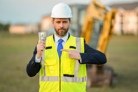Successful business. Financial investment. Money budget. Successful construction investor man point finger on money. Businessman count money at site. Businessman invest money in construction businessの写真素材