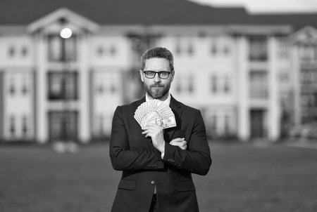 Successful realtor in suit with money dollar. House owner hold money outdoor. Realtor offering new home. Broker make offer. Businessman broker with money. Property concept. Licensed real estate agentの写真素材