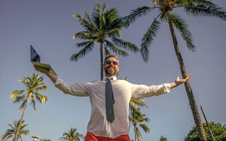 Business man using laptop near palm tree. Business trip. Man freelance work online at beach....