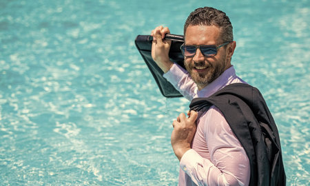 Freelancer has remote work. Businessman in suit with briefcase at swimming pool. Successful freelancer. Business trip success. Business retreat. Happy businessman on summer vacation, copy spaceの写真素材