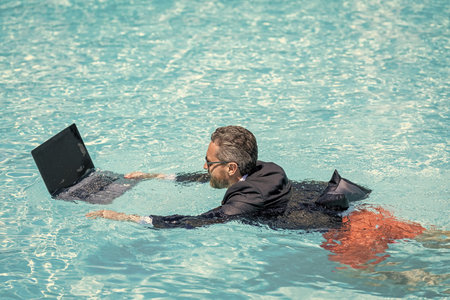 Man using laptop for freelancing in pool. Business freelancing. Businessman on summer vacation. Businessman using webcam for video. Freelance man has online video call. Freelance working onlineの写真素材