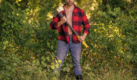 Lumberjack man with axe. Lumberjack axe. Man with logging axe. Man in unbuttoned shirt. Lumberjack hardworking outdoor. Cropped viewの写真素材