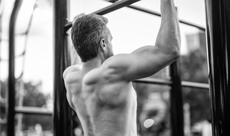 Man sportsman do pulling exercise. Man muscular back athlete pull up in outdoor gym. Sport...