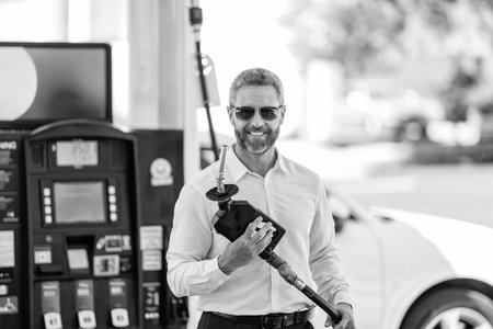 Businessman in sunglasses refueling car in petrol gas station. Entrepreneur standing at petrol...