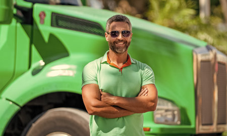 Handsome man driver in front of green truck. Trucking owner. Truck driver. Man trucker driver near...