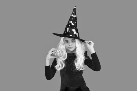 Witch All Hallows costume of girl. October 31 pumpkin. Costume party. Halloween pumpkin in hand of witch girl. Halloween witch girl isolated on orange. Pumpkin on Halloween. Harvest festivalの写真素材