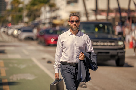 Successful businessman walking with briefcase outdoor. Businessman hold briefcase. Businessman after...