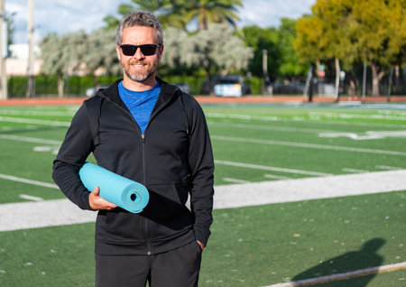 Sport man ready for workout. Healthy lifestyle. Fitness and sport. Yoga mat for training. Sportsman at stadium. Man in sportswear with fitness mat in stadium. Fit your body. Yoga coach
