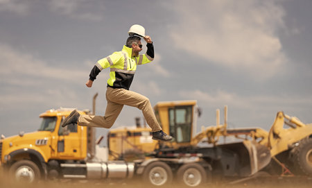 Man engineer running to success. Builder man run fast to work. Engineer supervisor running outdoor. Supervisor jumping. Excited construction builder. Worker jumping at heavy machinery