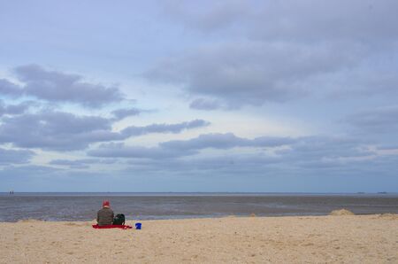 Lonely woman with a red hat is on vacation with a dog on the North Sea beach at low tide in the Wadden Seaの写真素材