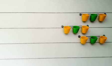 Yellow and green flowerpots were hang on railing and behind of them of is grey wall. This image took from wide angle and focusing on flowerpots at second row, the rest is blur.の写真素材