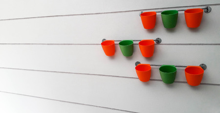 Orange and green flowerpots were hang on railing and behind of them of is grey wall. This image took from wide angle and focusing on flowerpots at second row, the rest is blur.の写真素材