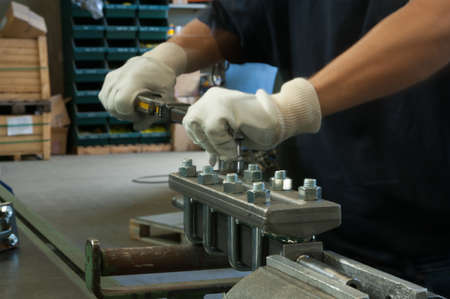 Mechanic in a steel plant working with a wrench on a metallic table.