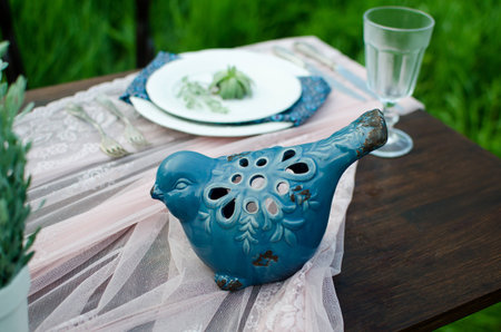 Close up vintage bird. Wedding decoration table in rustic style on green grass. Close up of dark wooden table, white tablecloth, dishes and crystal glasses. Pot with green flowers and decoration. の写真素材